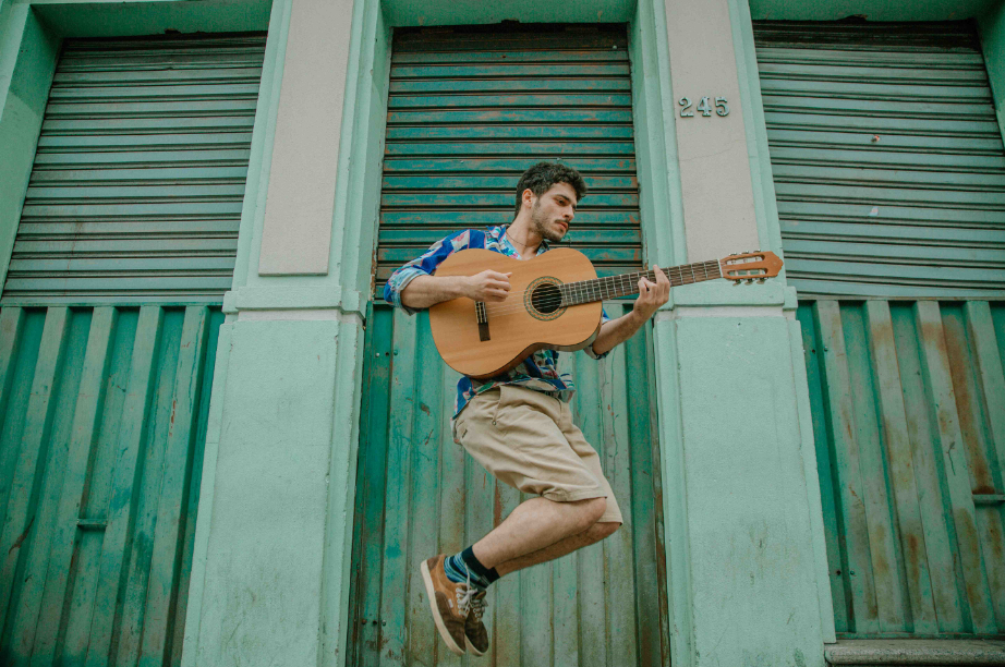 O músico Lucas Ucá estão com seu violão nas mãos enquanto salta no ar