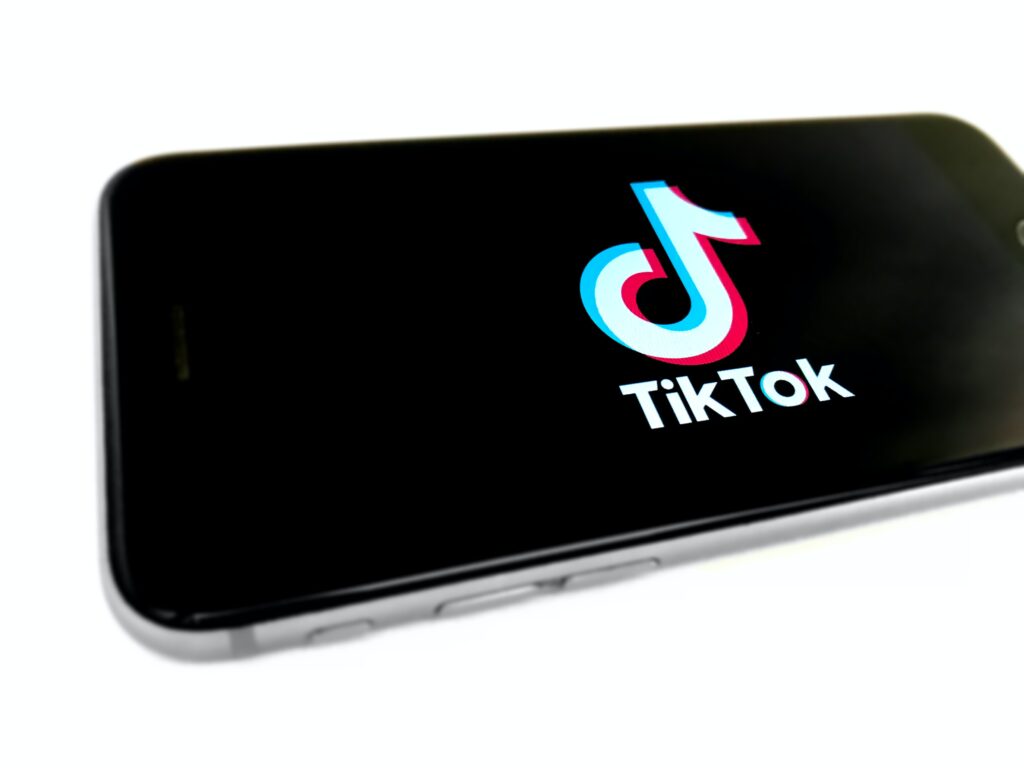 Imagem de um celular posicionado sobre a superfície na horizontal. Na tela do aparelho, o fundo preto destaca a logo do aplicativo TikTok